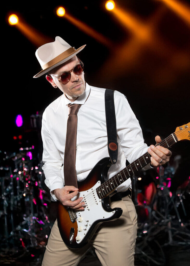 Sandy Leresche à la guitare devant la batterie, sous des lumières orange