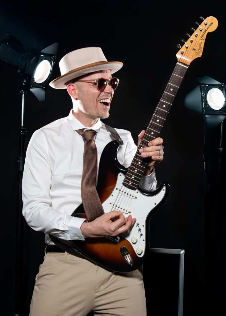 Sandy Leresche rit en jouant de la guitare sur scène