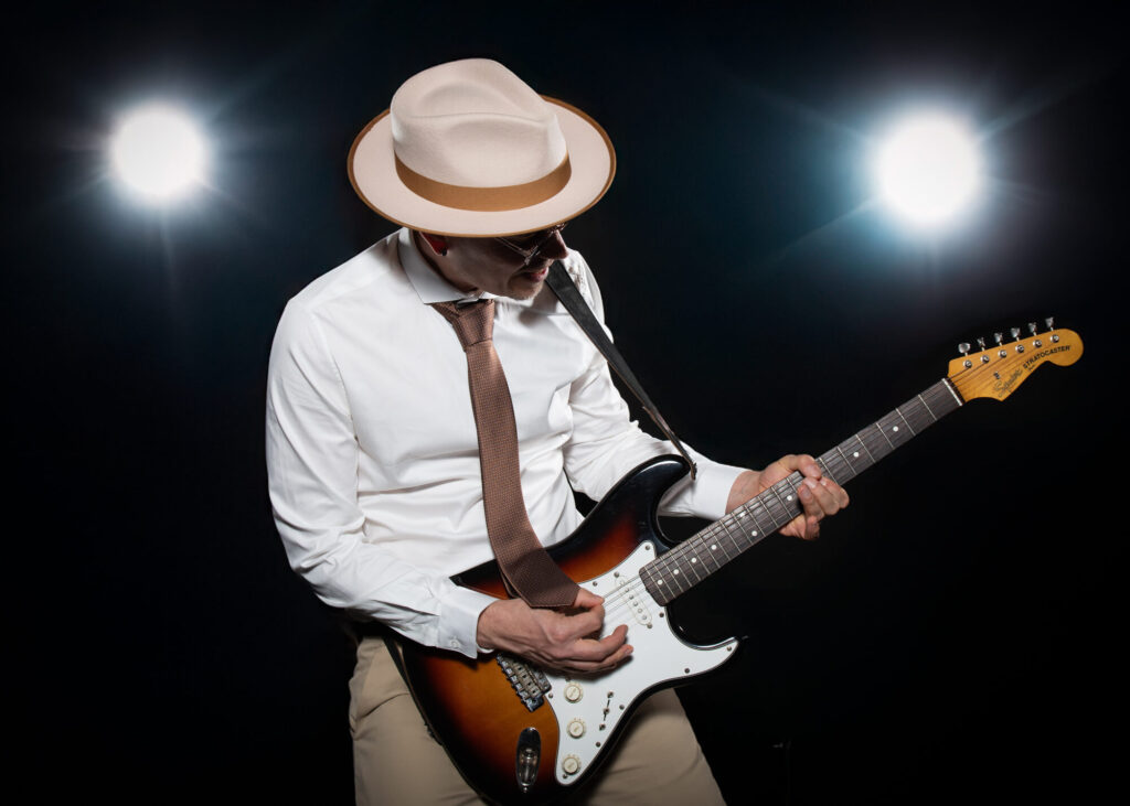 Sandy Leresche concentré sur son manche de guitare, deux projecteurs en fond
