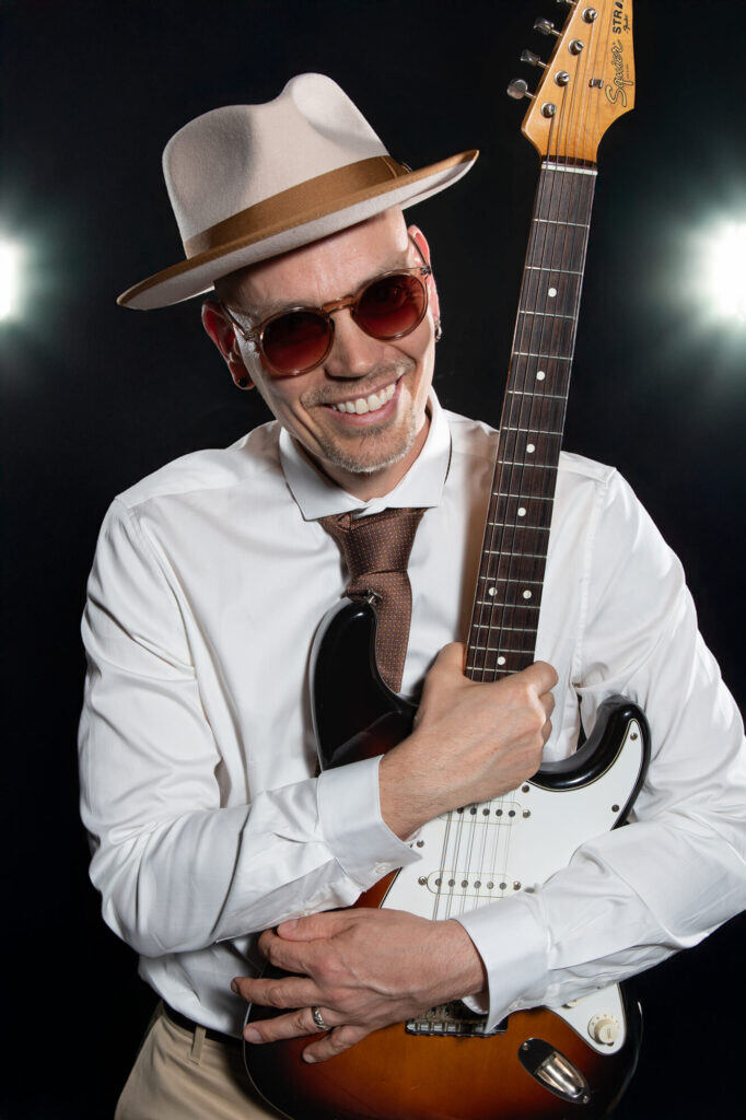 Sandy Leresche serre sa guitare électrique contre lui, chapeau blanc et lunettes teintées